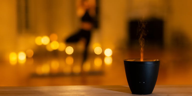 Aroma diffuser Zoe in black from Stadler Form shines while woman practices yoga in the background Aroma diffuser Zoe in black from Stadler Form shines while woman practices yoga in the background