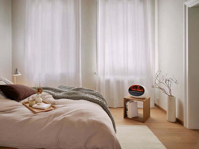 Erik fan heater with flame effect by Stadler Form in a bright bedroom