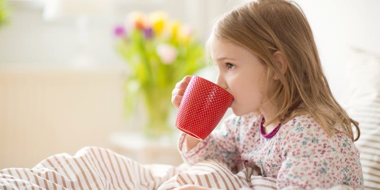 Fille assise malade au lit avec une tasse de thé Fille assise malade au lit avec une tasse de thé