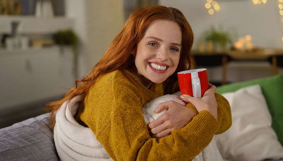 A woman on a sofa snuggles happily into a blanket