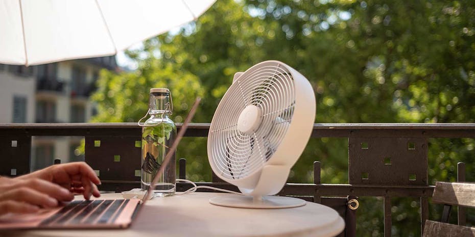 Tim table fan by Stadler Form in white next to a laptop on a balcony