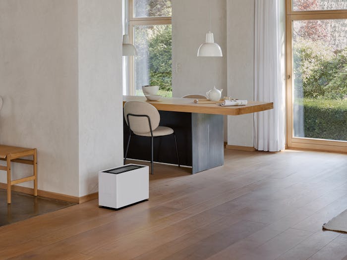 Noah Pro humidifier by Stadler Form in a large, open living area between the coat rack, dining table, and seating area.