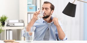 A man sweats in the office at work and drinks water. A man sweats in the office at work and drinks water