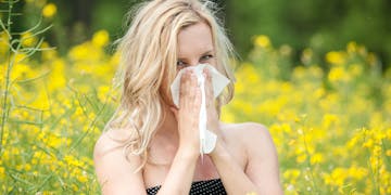 Frau, die sich vor einer Blumenwiese die Nase putzt