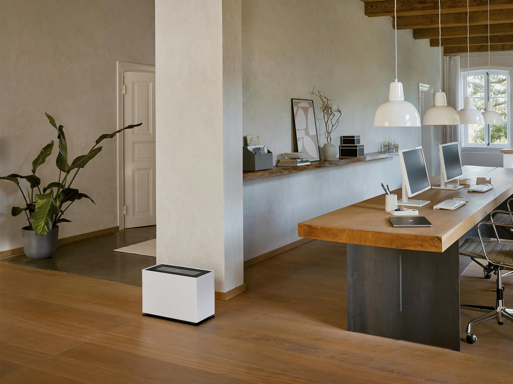 Noah Pro humidifier by Stadler Form next to a long solid wood desk with two workstations.
