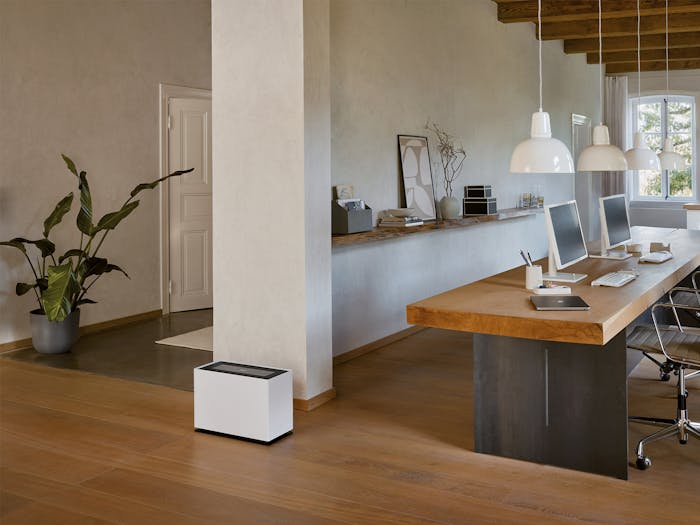 Noah Pro humidifier by Stadler Form next to a long solid wood desk with two workstations.