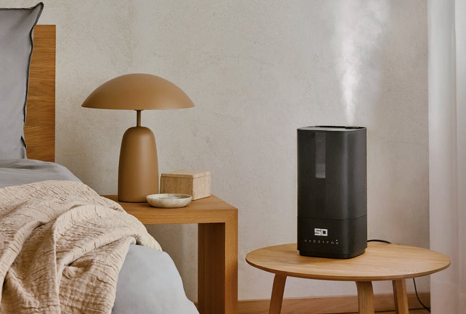 Humidificateur Oliver de Stadler Form posé sur une table d'appoint à côté d'un lit